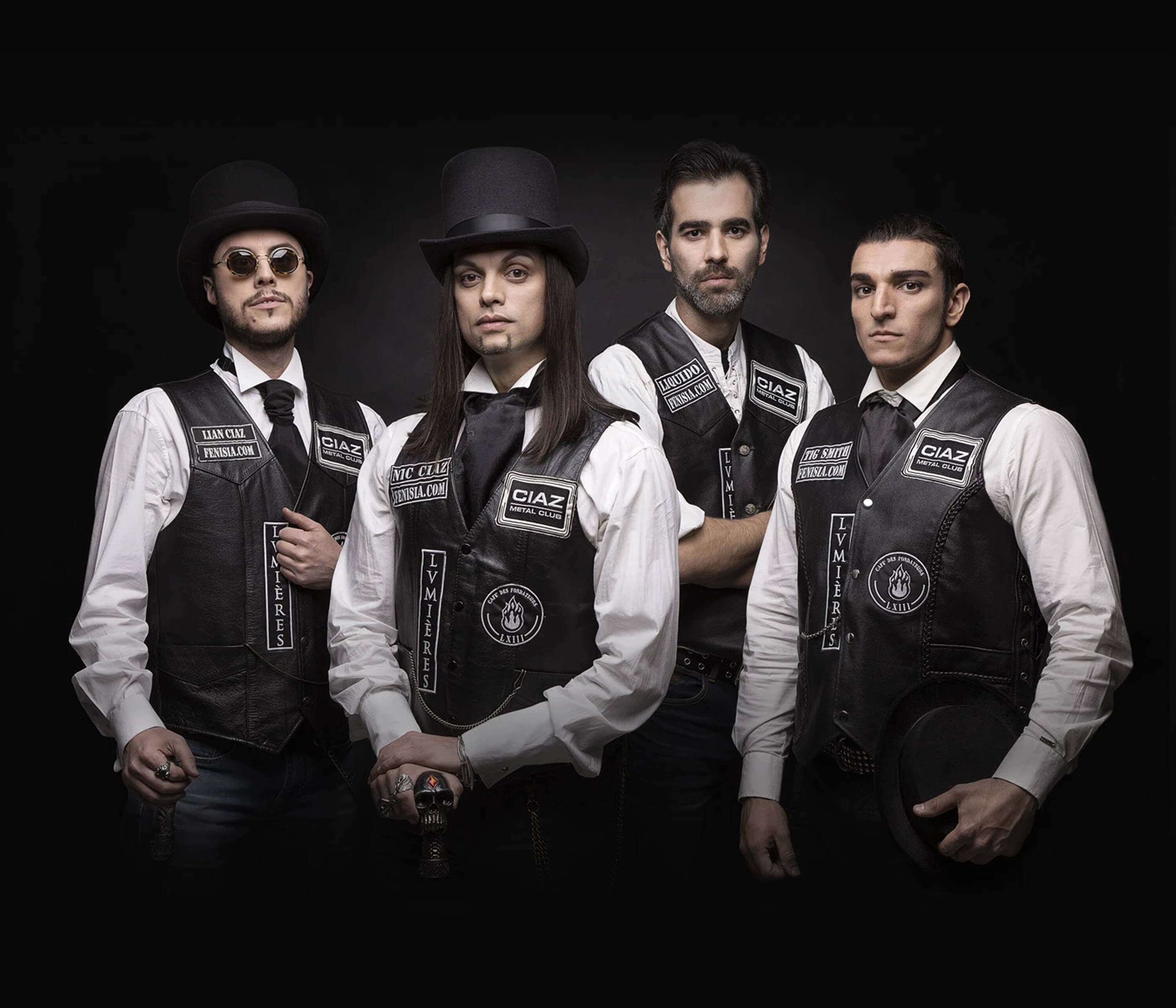 Group portrait against black — the four members in top hats, round glasses and patched leather waistcoats, one holding a skull ring, one holding his hat