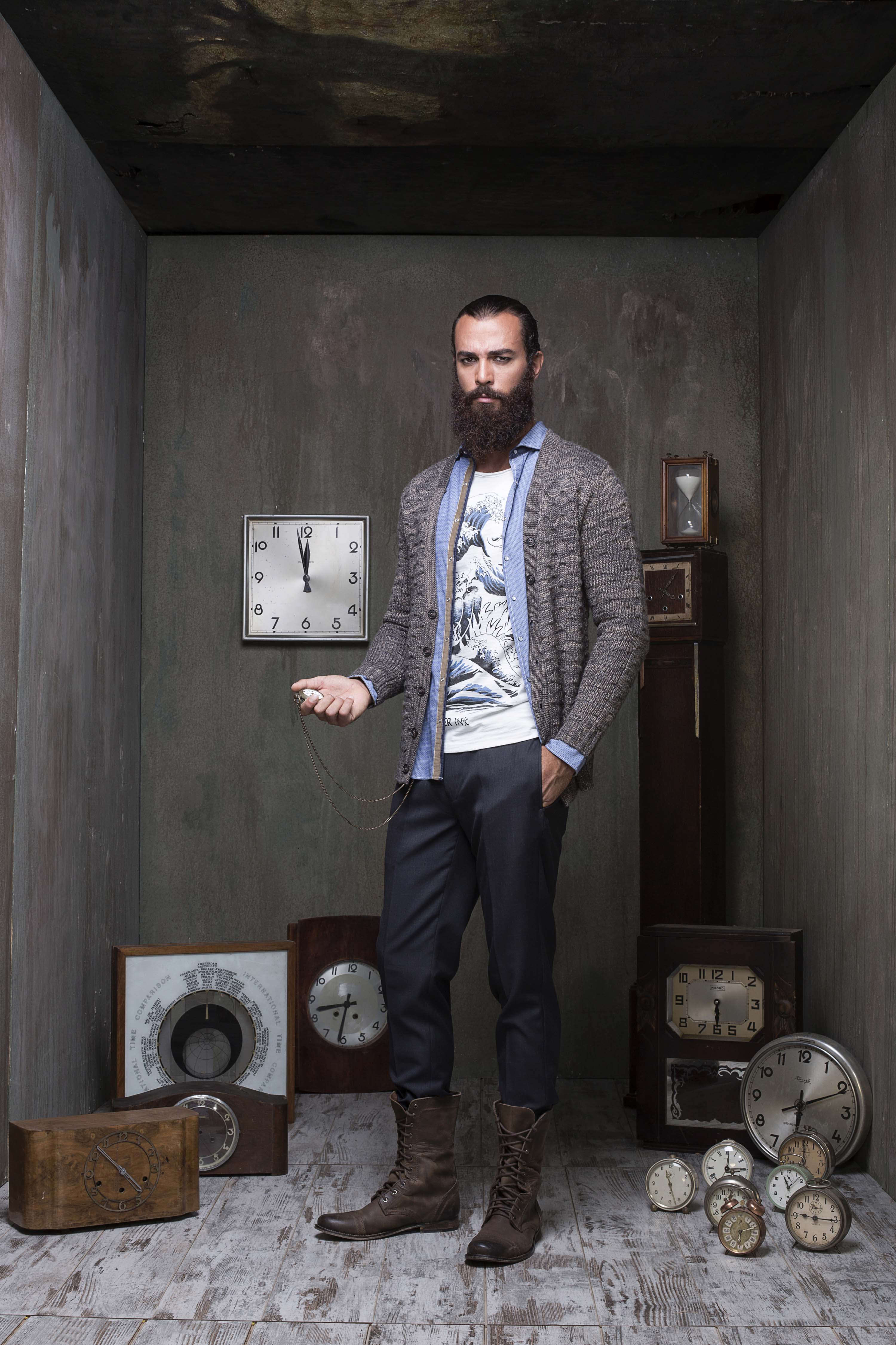 Grey cardigan over a wave-print tee, holding a pocket watch, surrounded by antique clocks and barometers