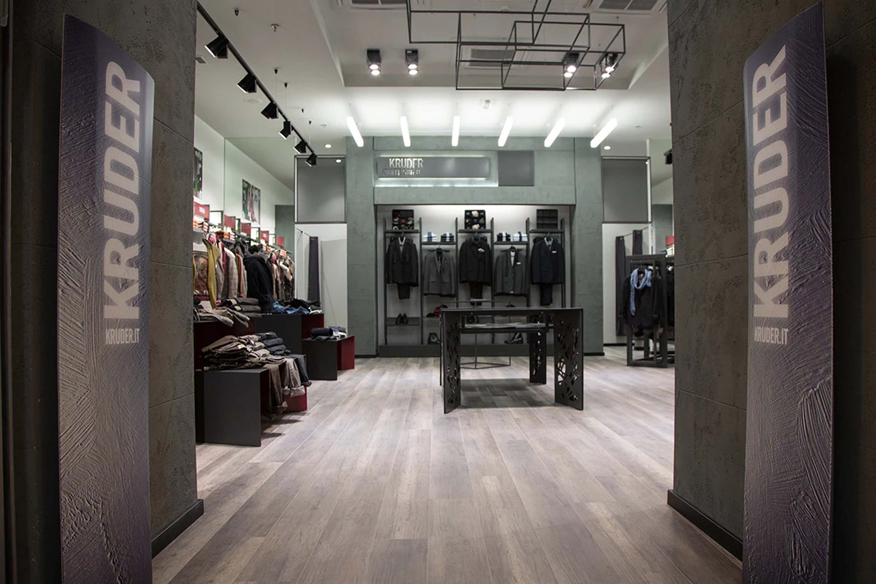 The Kruder store interior — suits and knitwear on grey concrete walls, branded pillars