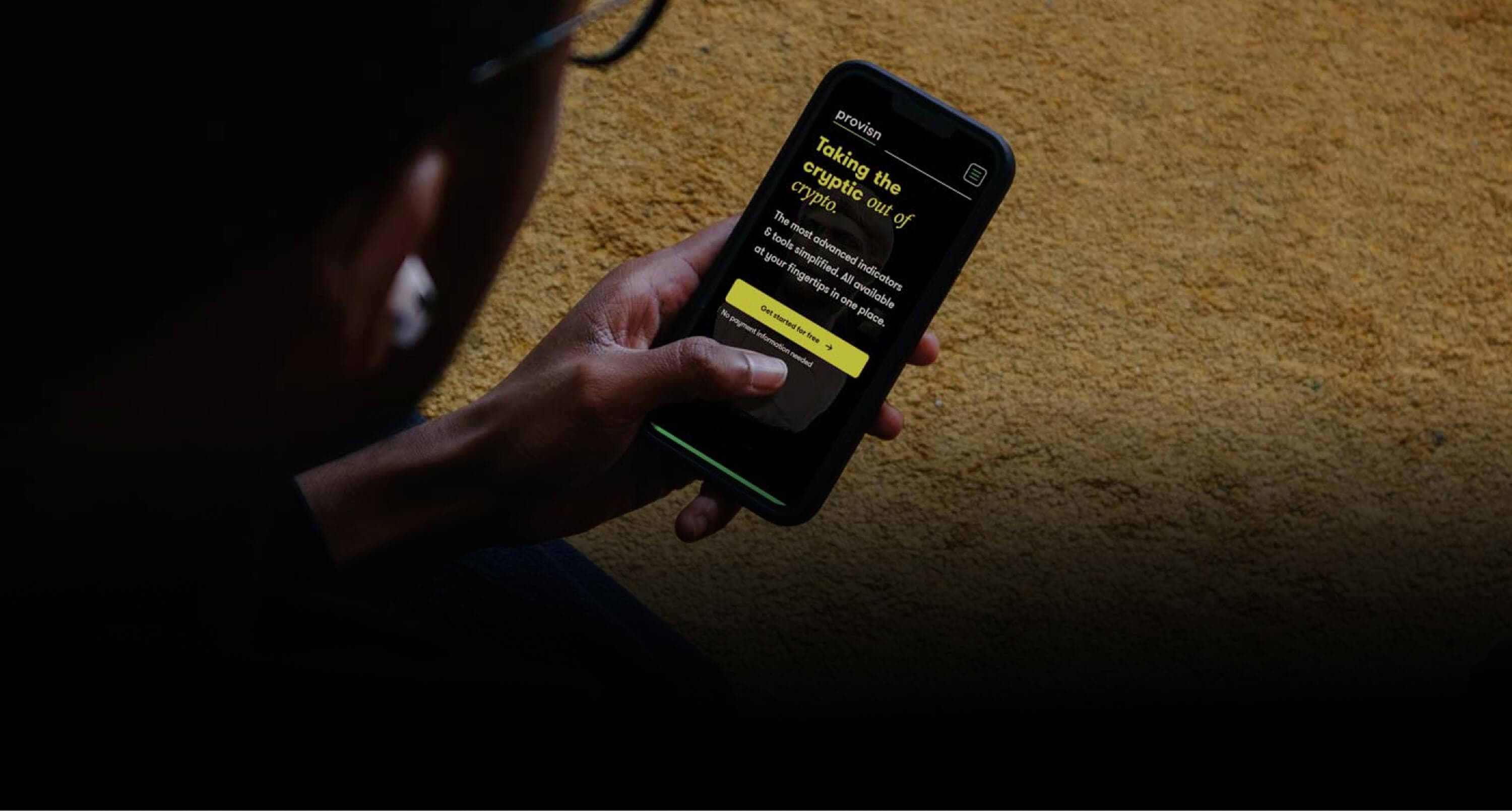 The landing page seen over the shoulder of someone holding a phone against a yellow wall, with the headline and the call to action on screen