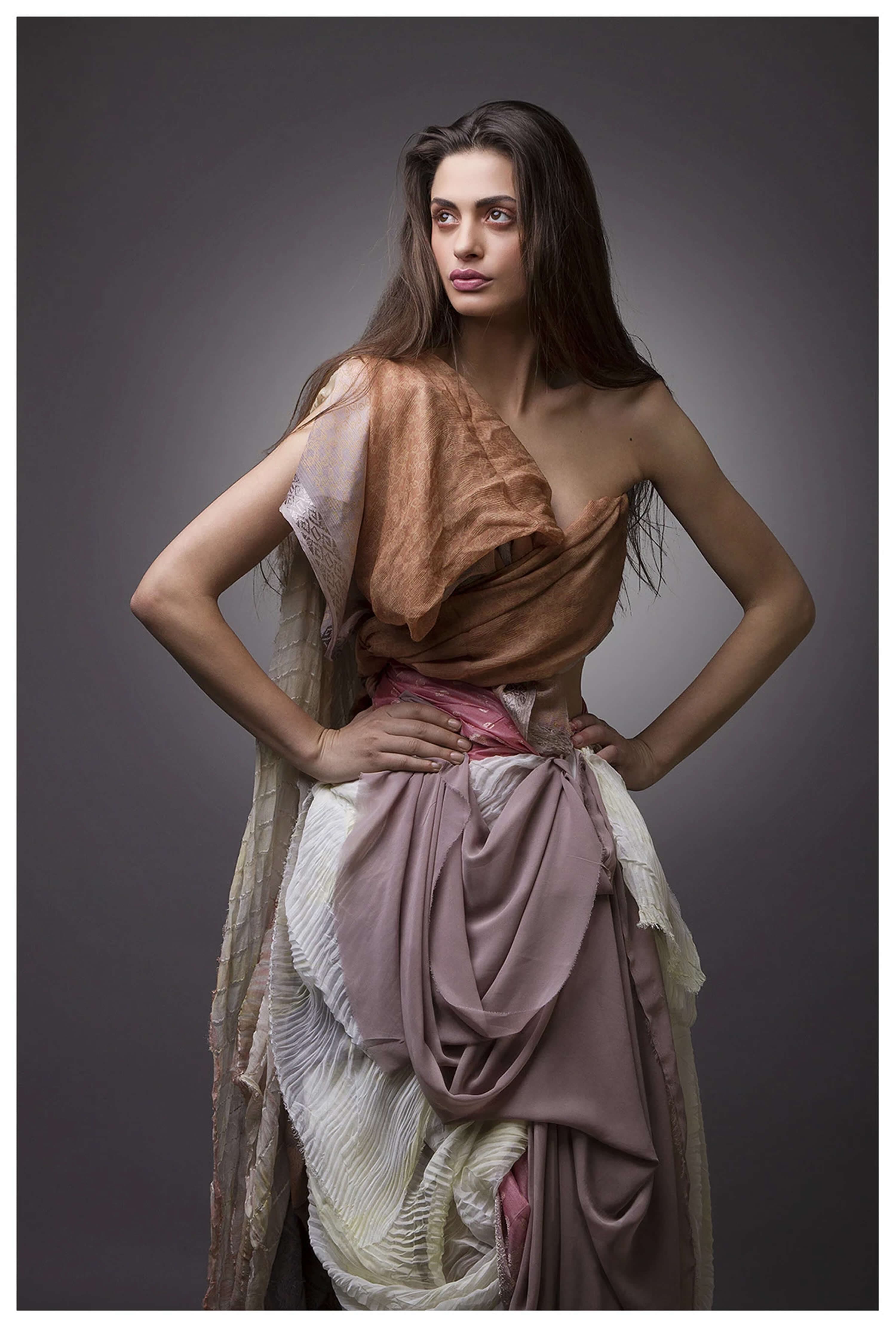 Standing look — copper silk wrapped asymmetrically over one shoulder, a pink sash at the waist and a full skirt of layered mauve, cream and pleated silks