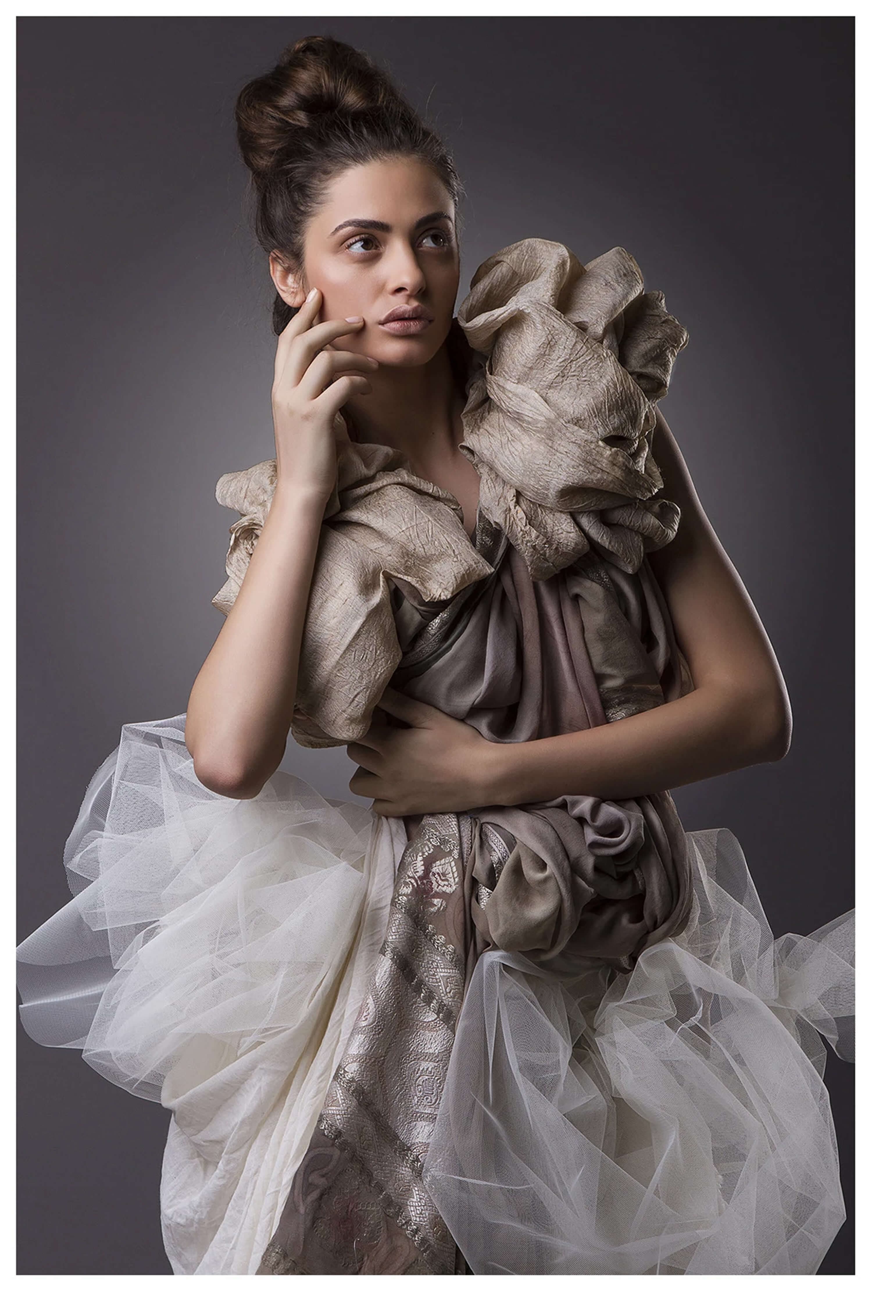 Sand-coloured silk with a sculptural shoulder rosette over a mauve drape, worn with a full white tulle underskirt, hand raised to the face