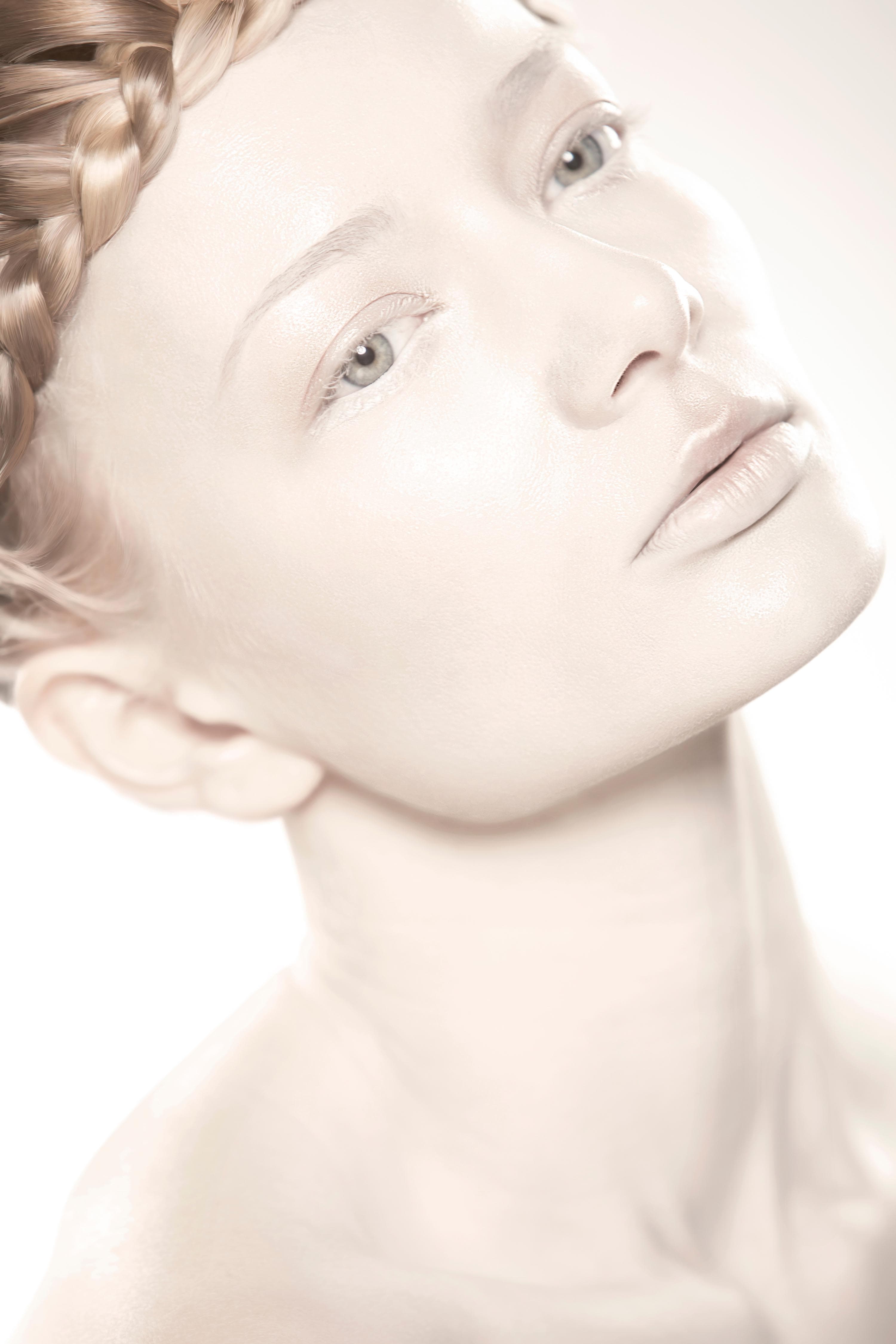 High-key beauty portrait — luminous pale skin and a crown braid, looking upward, on white