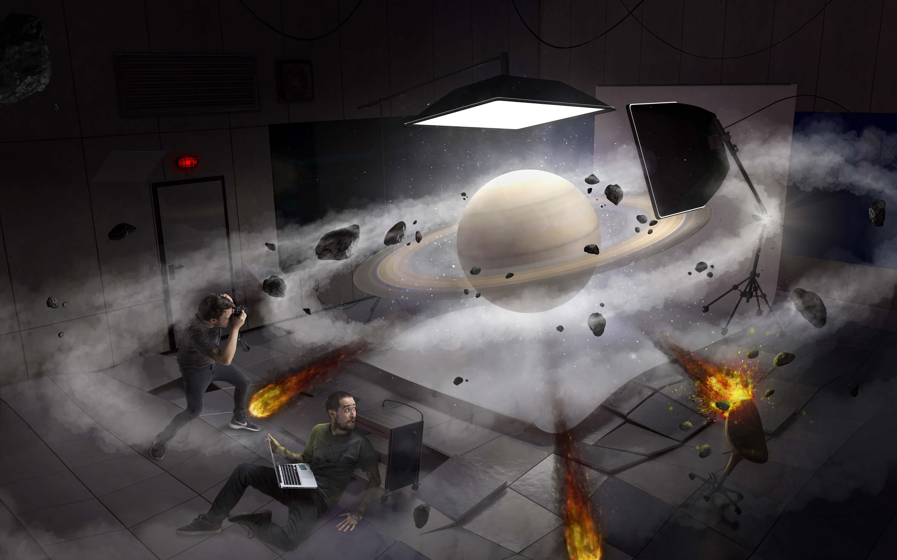 Saturn, the finished image — the ringed planet suspended in the middle of the studio inside a cloud of dust and asteroids, one photographer shooting crouched by the door while his assistant falls backwards with a laptop, a meteor burning across the floor and another exploding against a stool