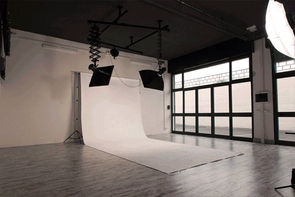 Looping animation in which a blue wave rises out of the white cyclorama of the Phorma studio, between two softboxes on a ceiling rig and tall factory windows