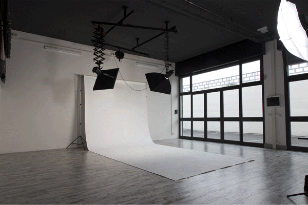 Looping animation of the Phorma studio in daylight, a blue wave rising out of the white cyclorama between the softboxes and the tall windows